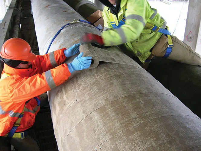 Men applying Denso tape onto pipe